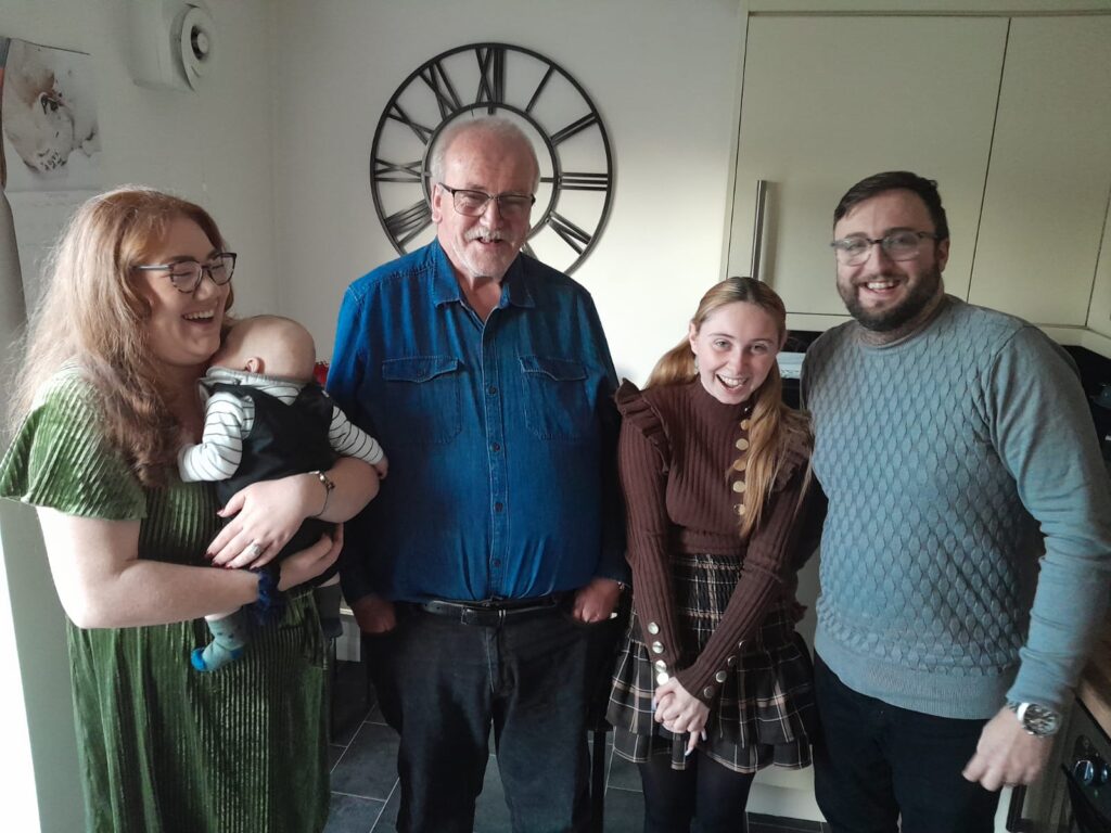 A Shared Lives famil shot - this time Beth is holding her and Craig's baby, Anthony, and the family are stood laughing in their kitchen