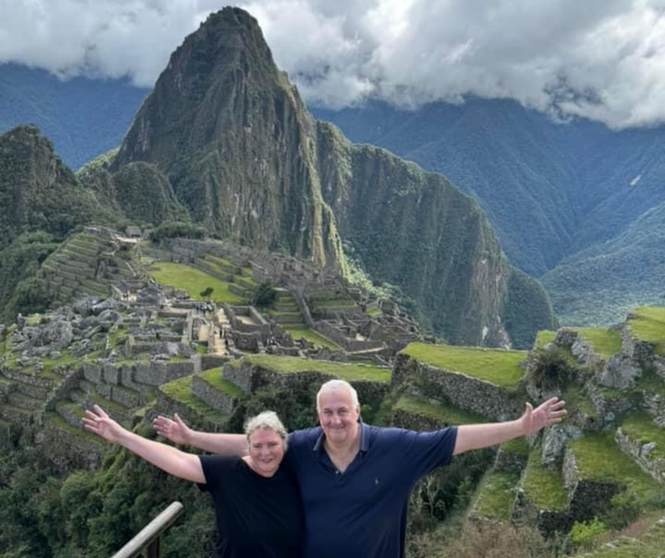 Paul and Kath stand with arms out stretched in front of the incredible Inca trail in Peru