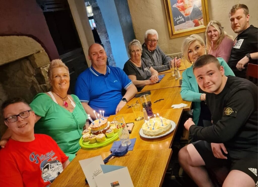 The whole family, including Phil who they support, their son Jayden and the grandparents are all gathered around a table together looking friendly and warm.