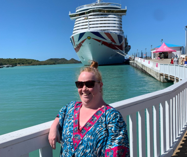 Victoria is standing in front of a huge cruise boat, which she's spending her holiday on! She is smiling brightly and wearing a colourful kaftan so they must be somewhere hot!